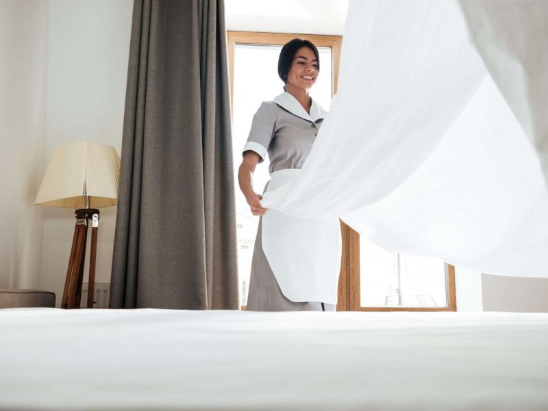 Young hotel maid changing bed sheets